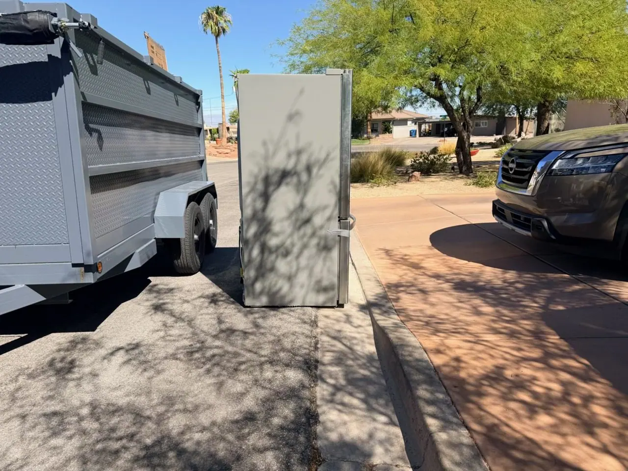 Old refrigerator set out at the curb beside the Henderson Junk Solutions trailer for appliance removal