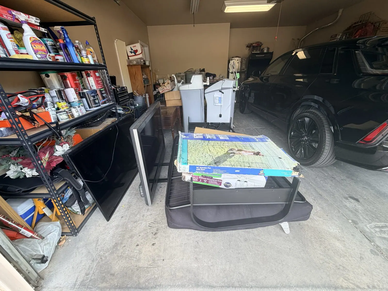 Garage with old flat-screen TVs, a pet crate and boxed items blocking the parking bay before a garage cleanout